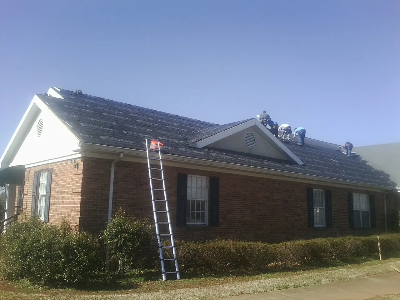 Crew tearing shingles off a brick ranch roof with a ladder set — Metal Roof Repair work by our crew in Nashport
