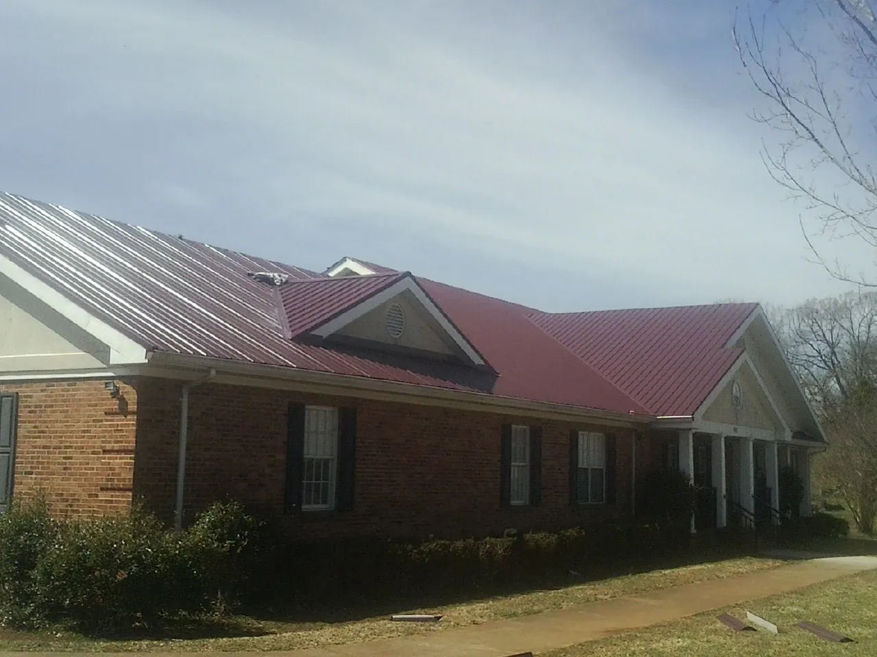 Red metal roof with gabled entries on a long brick building, from a Hail Damage Roof Repair job in Nashport