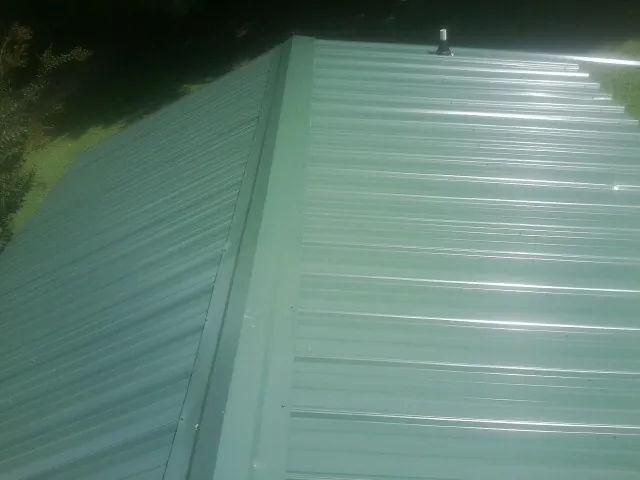 New green metal panels meeting at the ridge of a roof — Flat Roof Repair work by our crew in Nashport
