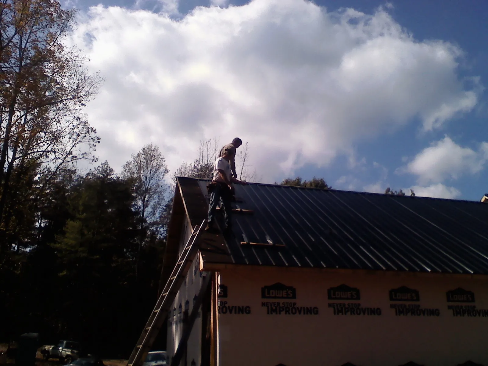 Roofer fastening dark metal panels high against a cloudy sky, from a Roof Inspection job in Nashport