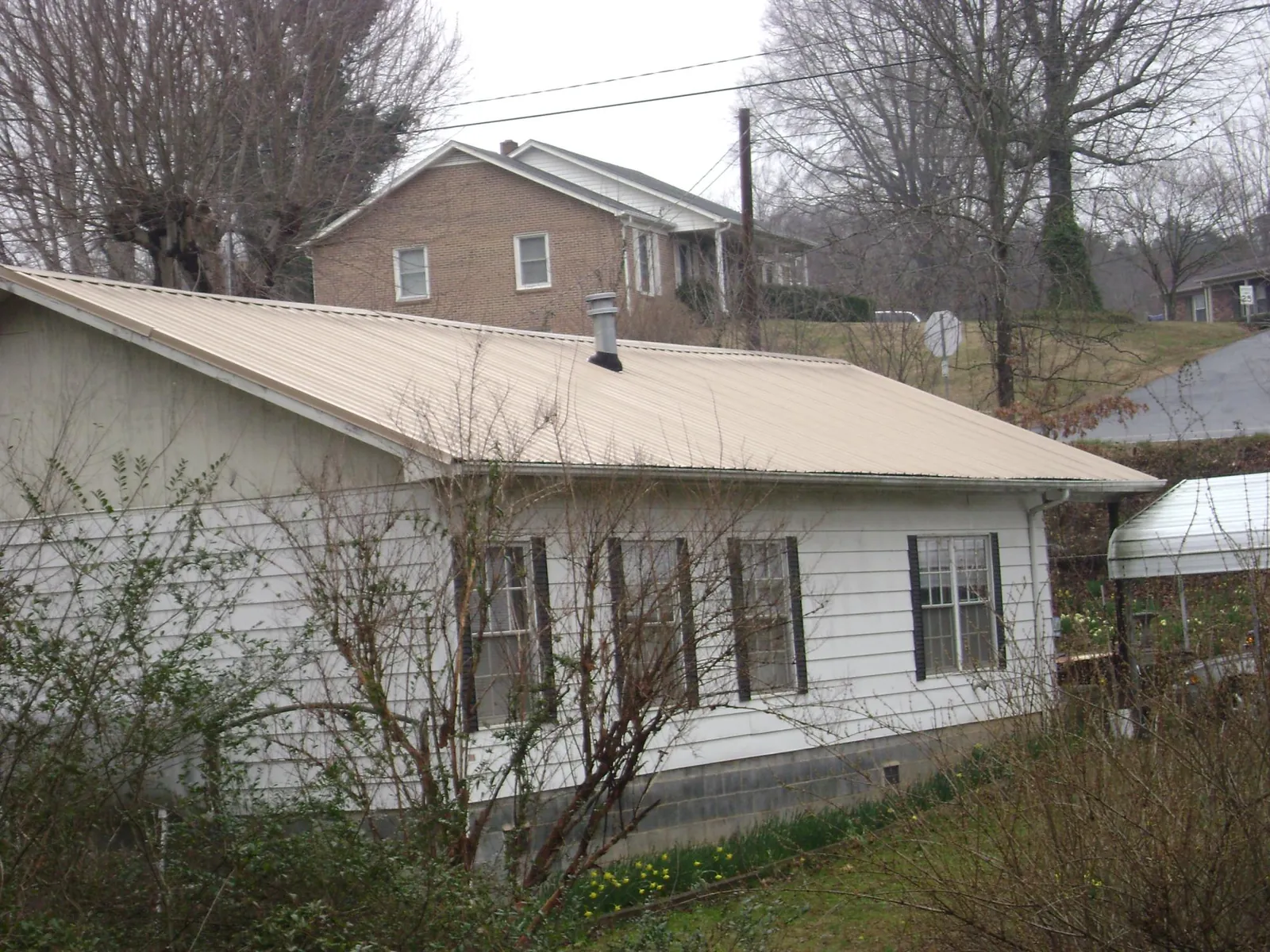 Tan metal roof on a white sided house set into a hillside — Commercial Roofing by Roofing Brothers in Nashport